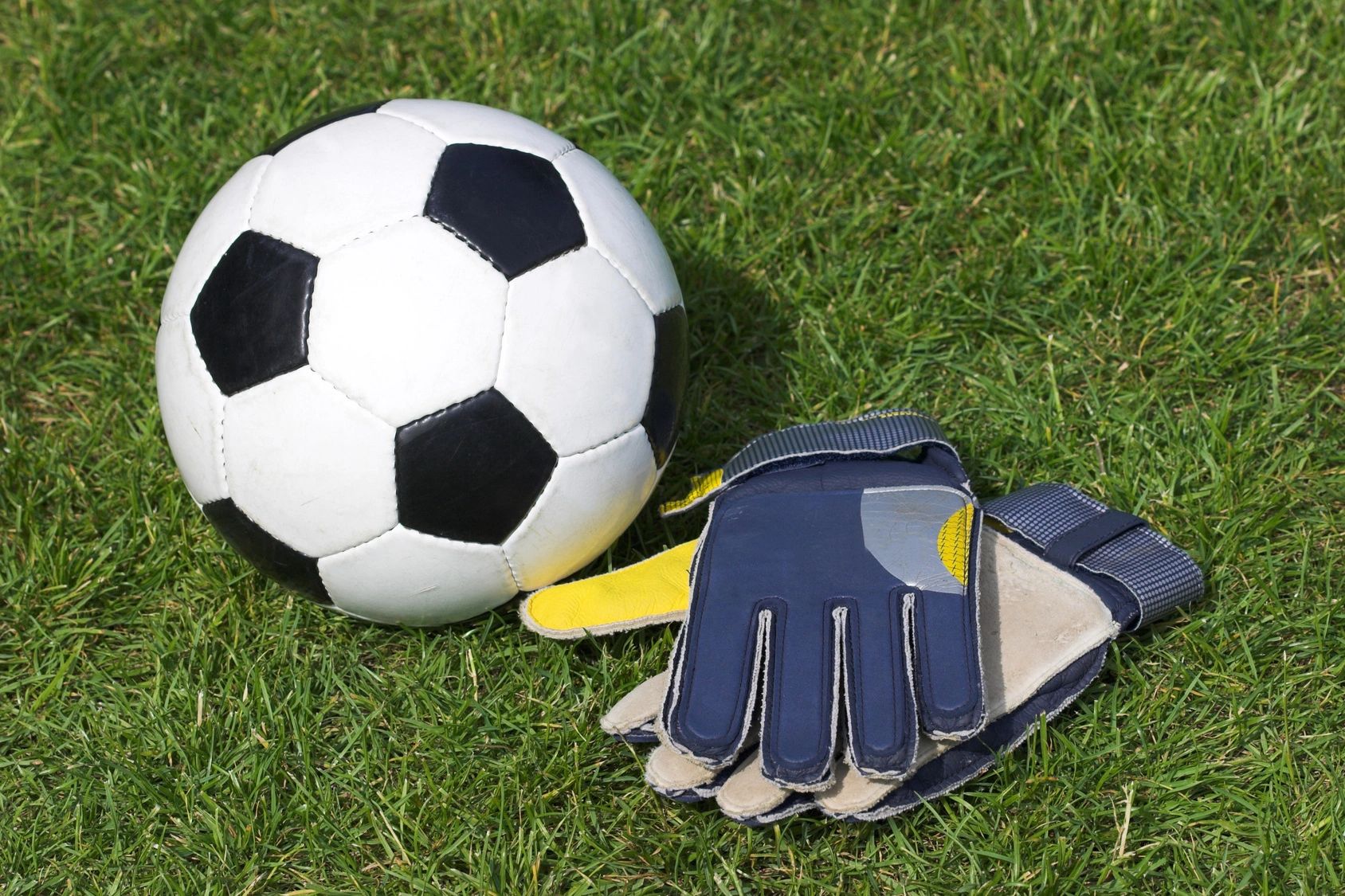 Soccer ball on grass with goalkeeper gloves